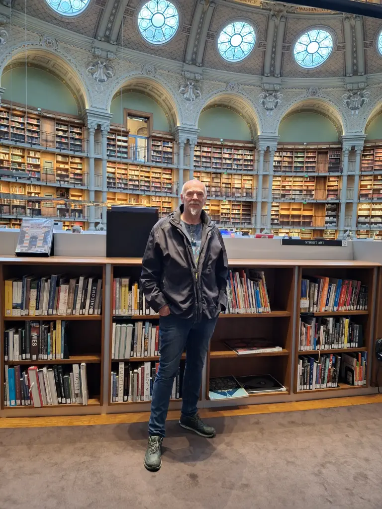 Autor Tom Wahlfeld in der Französischen Nationalbibliothek, stehend vor hohen Bücherregalen im historischen Lesesaal