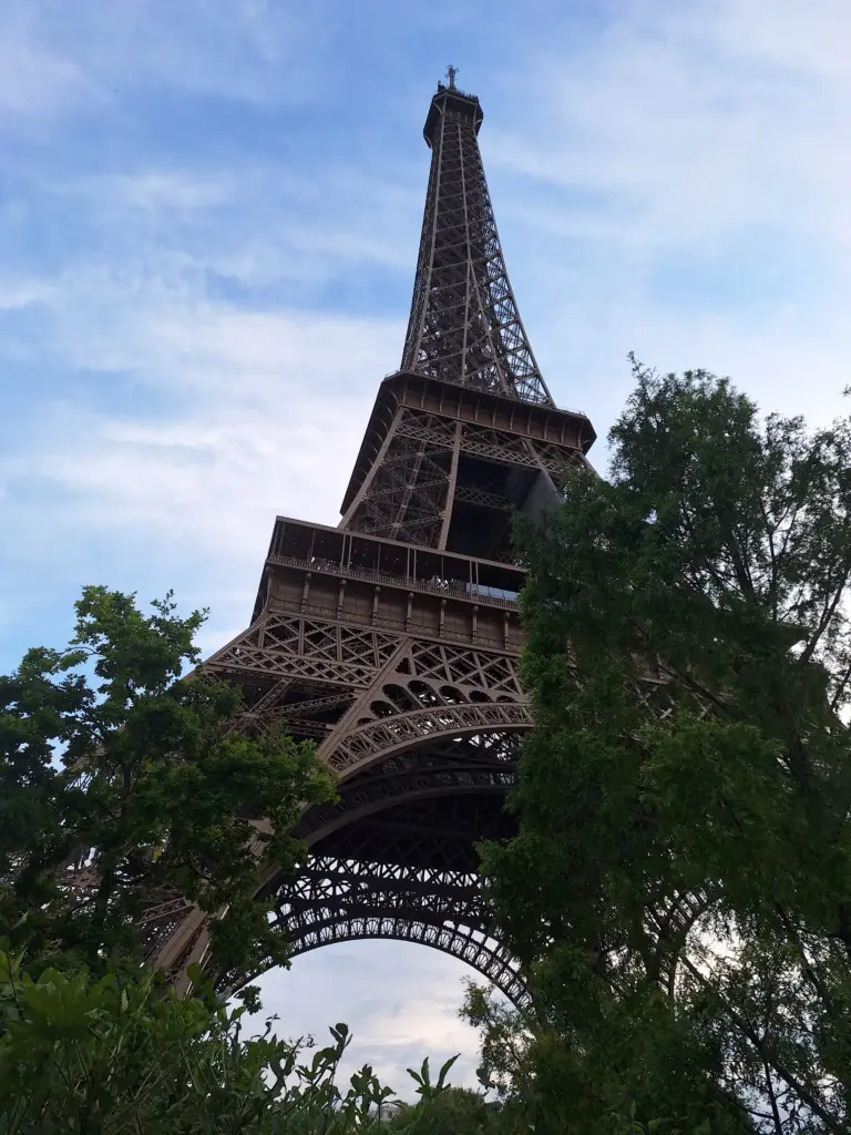 Blick auf den Eiffelturm von unten, eingerahmt von Bäumen, bei leicht bewölktem Himmel in Paris